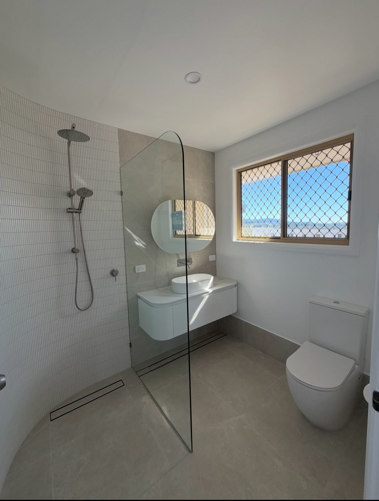 Curved tiled wall shower, vessel sink vanity and toilet in a finished bathroom
